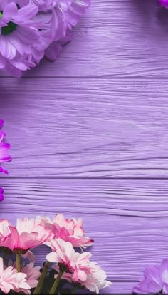 pink and purple flowers are arranged on a wooden background with space for text or image