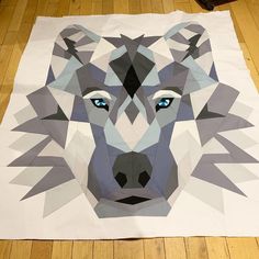 a wolf made out of paper sitting on top of a wooden floor with blue eyes