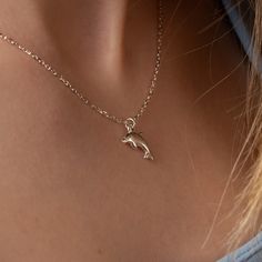 a woman wearing a necklace with a dolphin charm on it's back neck,