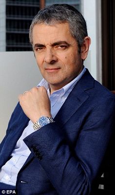 a man in a blue suit and white shirt is posing for the camera with his hand on his chin