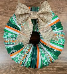 a wreath made out of green and white ribbons with a bow on the top, sitting on a wooden surface