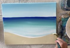 someone is painting a beach scene with blue and white watercolors on the canvas