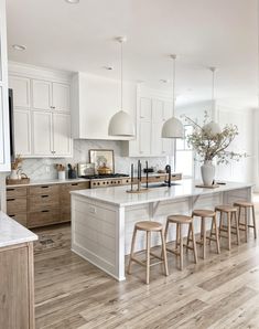 a large kitchen with white cabinets and wooden floors is pictured in this image, there are four stools at the center of the island