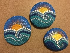 three painted rocks sitting on top of a table next to each other with waves and sun in them