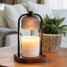 a lit candle sitting on top of a wooden table next to a potted plant