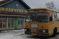 an old yellow bus is parked in front of a small building on a snowy day