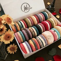 a box filled with lots of different colored macaroons next to flowers and candles