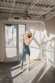 a woman is doing yoga in an empty room with sunlight streaming through the window and her hands behind her head