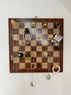 a chess board with jewelry hanging from it's sides on the wall next to a cell phone