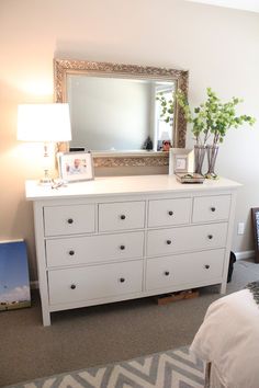 a bedroom with a white dresser and large mirror