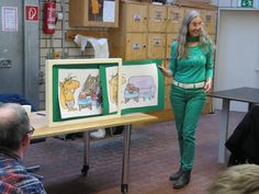 a woman standing in front of two pictures on a table with people sitting around it