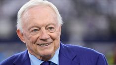 an older man wearing a blue suit and tie smiles at the camera while standing in front of a stadium