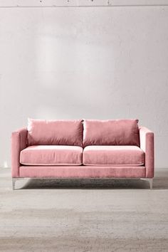 a pink couch sitting on top of a wooden floor next to a white brick wall