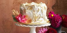 a white cake sitting on top of a table next to purple and red flowers in vases