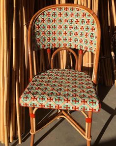 a wicker chair with an upholstered seat in front of bamboo poles and sticks