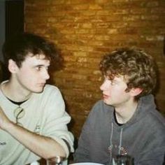 two young men sitting at a table with plates of food and drinks in front of them