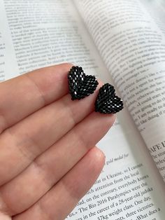 someone is holding their finger in front of an open book and wearing two black beaded hearts