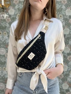 a woman wearing a white shirt is holding a black fanny bag with gold studs on it