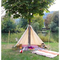 a teepee sitting under a tree next to a lake