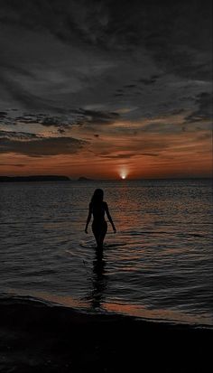 a woman walking into the ocean at sunset