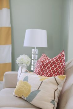 a white couch with pillows on it in front of a lamp and striped wallpaper