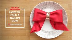 a white plate topped with a red bow on top of a wooden table next to a knife and fork