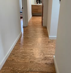 an empty hallway with white walls and wood flooring on the other side, leading to another room