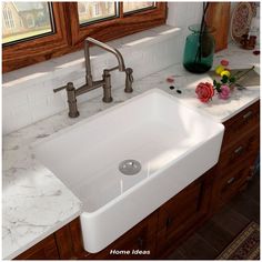 a white kitchen sink sitting under a window next to a counter with flowers on it