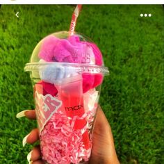 someone holding up a plastic cup filled with pink and white stuff on top of green grass