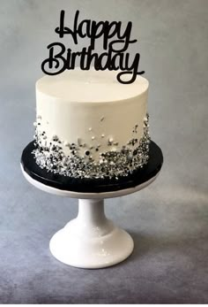 a white and black birthday cake sitting on top of a table with the words happy birthday written on it