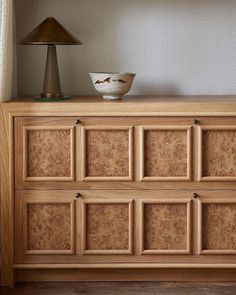 a wooden dresser with a lamp on top of it next to a wall mounted shelf