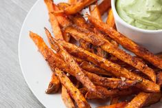 a white plate topped with sweet potato fries and guacamole dipping in a small bowl