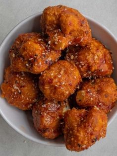 a white bowl filled with fried meatballs covered in sesame seeds on top of a table