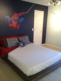 a bedroom decorated in blue and red with a spiderman wall decal on the wall