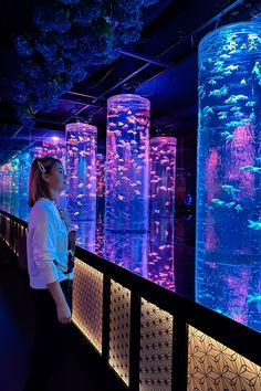 a woman standing in front of a large aquarium filled with blue and pink fish at night