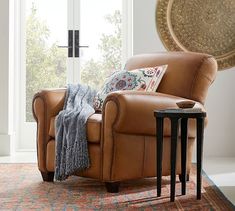 a brown leather chair sitting in front of a window next to a table with a blanket on it