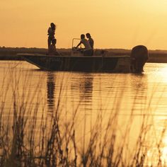 three people on a boat in the water at sunset