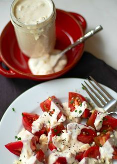 a white plate topped with tomatoes and cheese next to a cup of cream sauce on a table