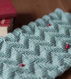 a knitted blanket sitting on top of a wooden table next to a red book