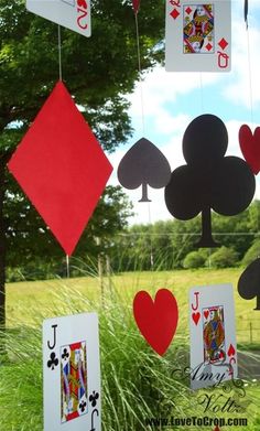 several playing cards hanging from strings in front of a tree and grass area with blue sky