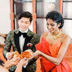 a man in a tuxedo handing food to a woman wearing an orange dress