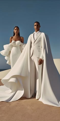 a man and woman dressed in white standing next to each other on top of sand dunes