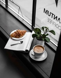 a cup of coffee and croissant sit on a window sill next to a book