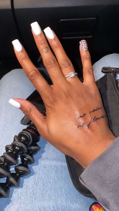 a woman's hand with a small tattoo on her left wrist and white nails