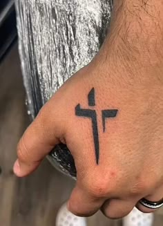 a person's hand with a cross tattoo on their left thumb and the middle finger