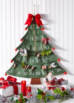 a christmas tree with presents around it on a table next to a white wall and red ribbon