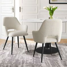 two white chairs sitting on top of a rug in front of a dining room table