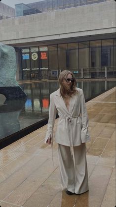 a woman walking down a sidewalk next to a statue in the middle of a city