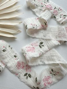 several pieces of cloth with pink roses on them next to an open book and fan