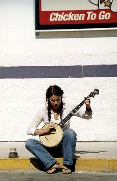 a woman sitting on the ground playing a musical instrument in front of a chicken to go store